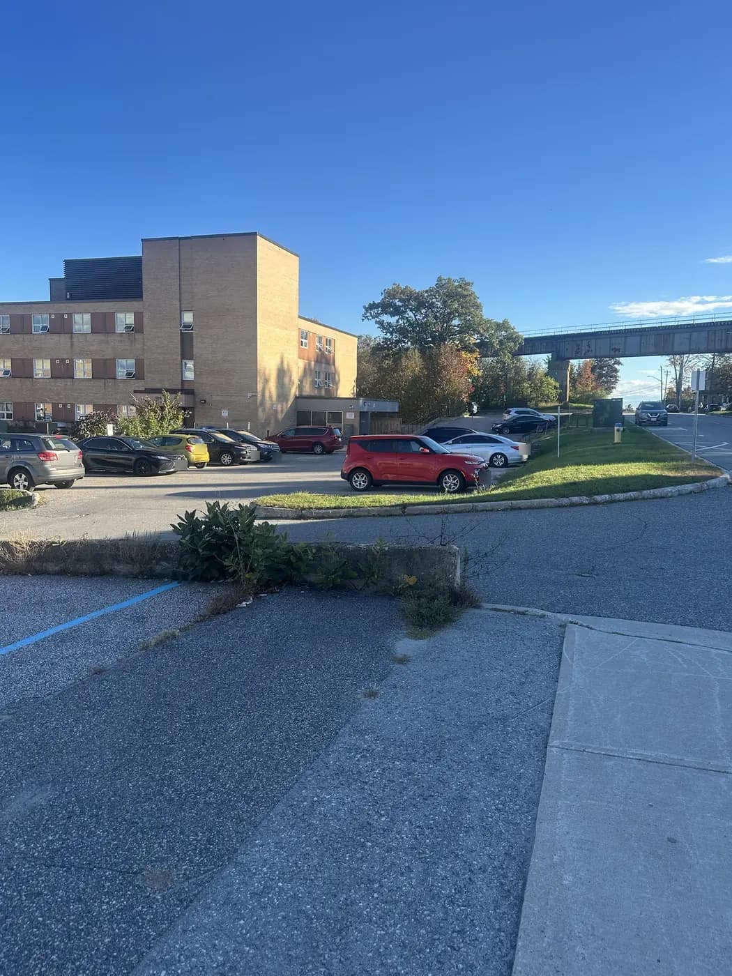 The tan brick apartment building at 31 Gibson Street seen from the sidewalk, with its parking lot in front and the railway bridge on the right.