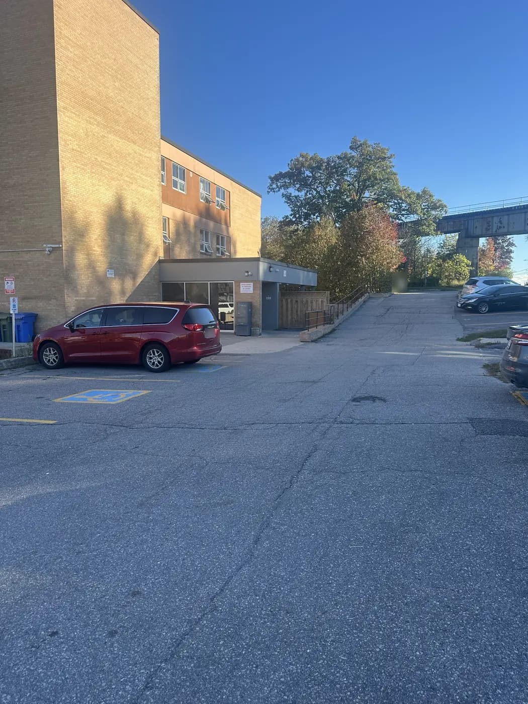 The low grey main entrance of the building seen from the parking lot, with a Canada Post mailbox beside the glass doors.