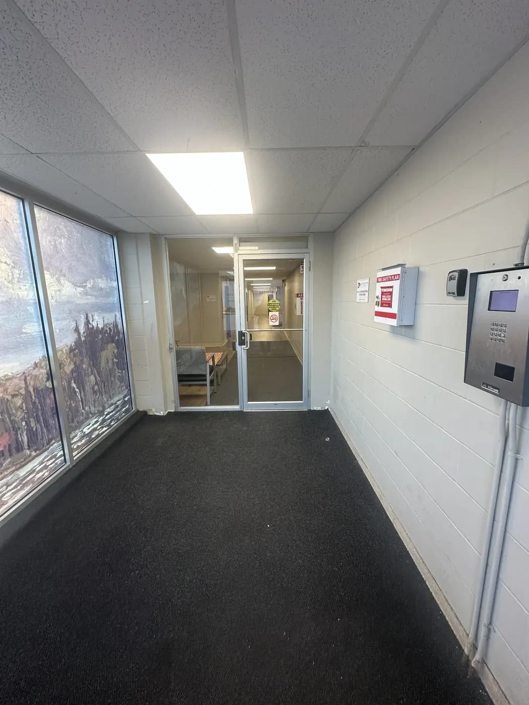 The small entrance area inside the front doors, with the silver buzz panel on the right-hand wall and a second glass door ahead.